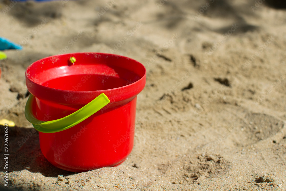 Baby red bucket with a green handle in the sandbox close up Baby red bucket with a green handle in the sandbox close up