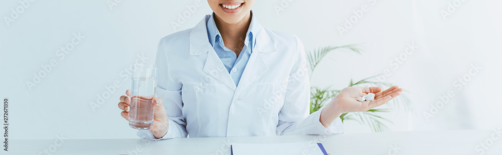 panoramic shot of smiling doctor with handful of pills and glass of water panoramic shot of smiling doctor with handful of pills and glass of water