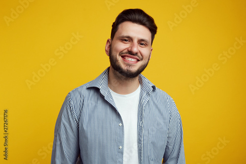 Attractive bearded young man laughing out loud, smiling broadly, showing his white straight teeth against yellow background