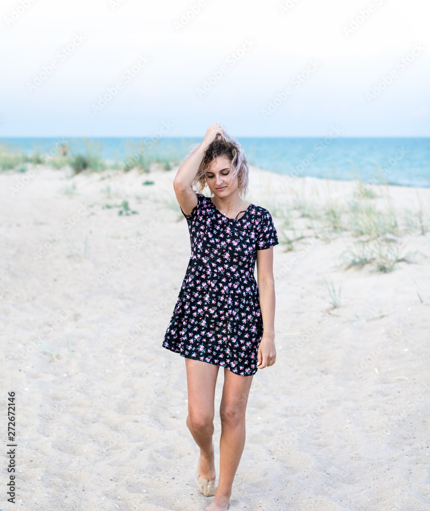 tanned beautiful young woman in cute dresswith flowers on the beach in clouds weather tanned beautiful young woman in cute dresswith flowers on the beach in clouds weather