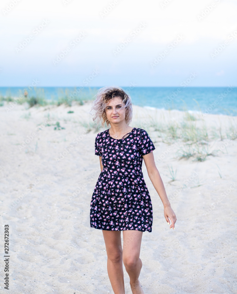 tanned beautiful young woman in cute dresswith flowers on the beach in clouds weather tanned beautiful young woman in cute dresswith flowers on the beach in clouds weather