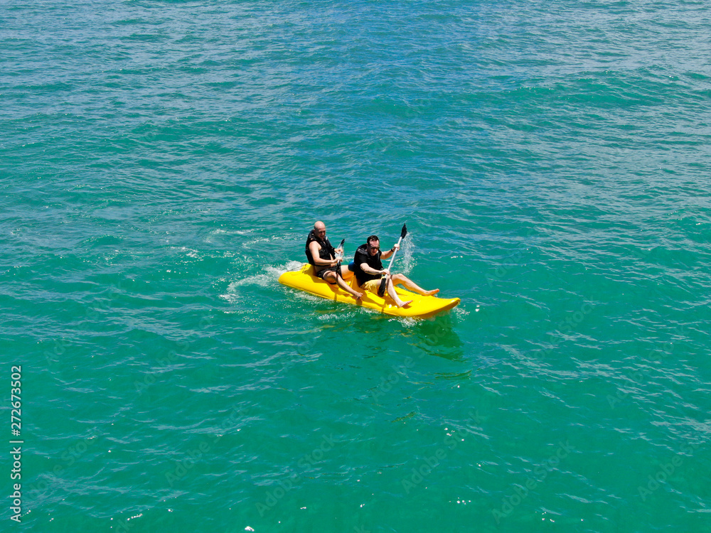 Fototapeta premium Aerial view of strong young active men kayaking on the clear blue turquoise water of the ocean. Active vacation. Praia do Forte, Brazil