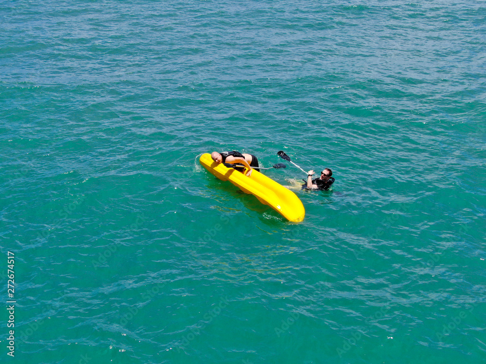 Aerial view of strong young active men capsizing with their kayak on the clear blue  turquoise water of the ocean. Active vacation. Praia do Forte, Brazil. 