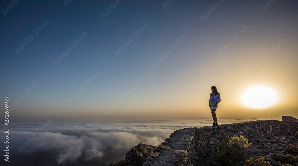 a woman on top of a mountain above the clouds during sunset