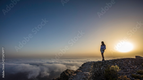 Obraz na płótnie a woman on top of a mountain above the clouds during sunset w salonie