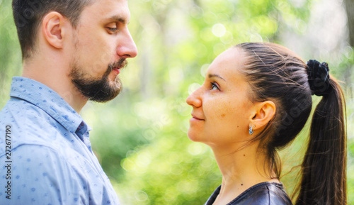 Outdoor portrait of a couple in love. Man and young woman with long ponytail hair look at each other