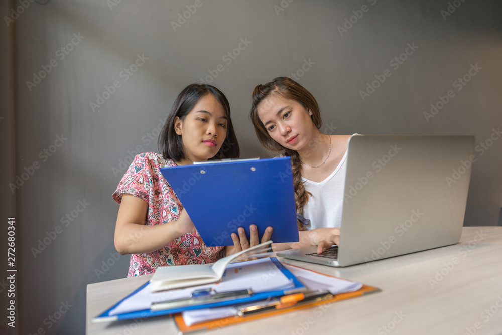 Two office ladies working on laptop and reading document report Two office ladies working on laptop and reading document report