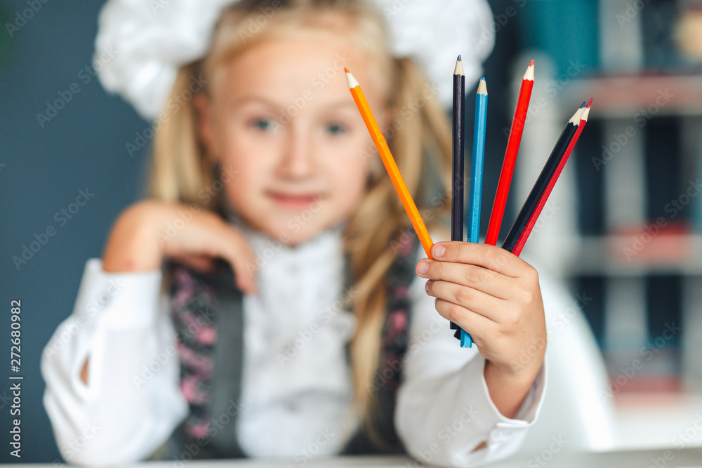 Close-up concept of colored pencils in the hands of a blondy schoolgirl who keeps them at face level at the table. A schoolgirl and a pencil. Look at the camera. Focus on pencils. Close-up concept of colored pencils in the hands of a blondy schoolgirl who keeps them at face level at the table. A schoolgirl and a pencil. Look at the camera. Focus on pencils.