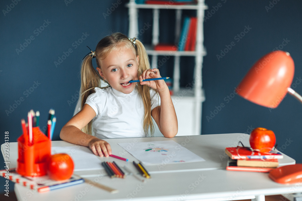 Funny little girl with blond hair sitting at white table and holding purple pencil in her mouth. Funny little girl with blond hair sitting at white table and holding purple pencil in her mouth.