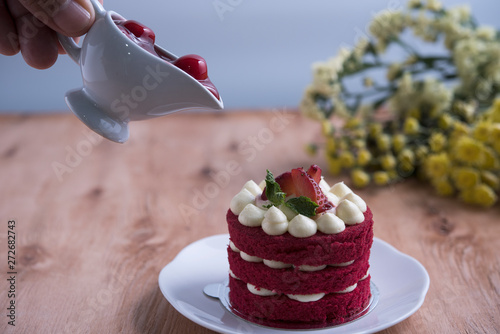 Piece of red velve cake on white plate decorated with strawberries put on the wood table.