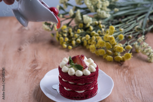Piece of red velve cake on white plate decorated with strawberries put on the wood table.
