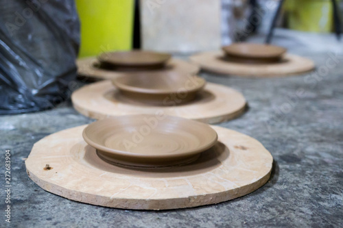 a master ceramist with 13 years of experience maked several plates from red clay on a potter's wheel, on a sheet of particle board for better removal and further drying. reportage