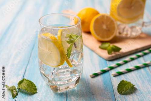 Fresh lemonade with lemon in glass on wooden background