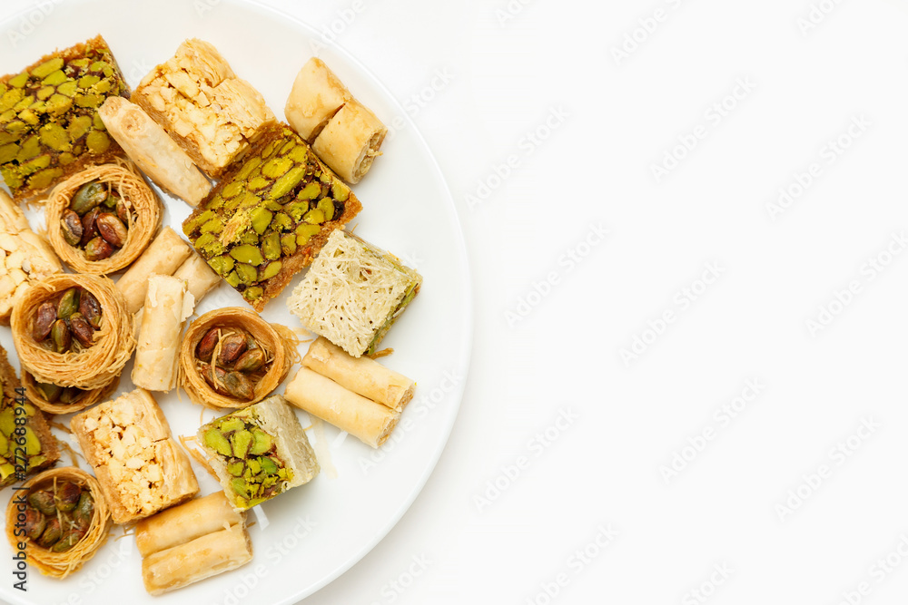 Traditional oriental sweets in white plate with different nuts on a white table, top view, copy space