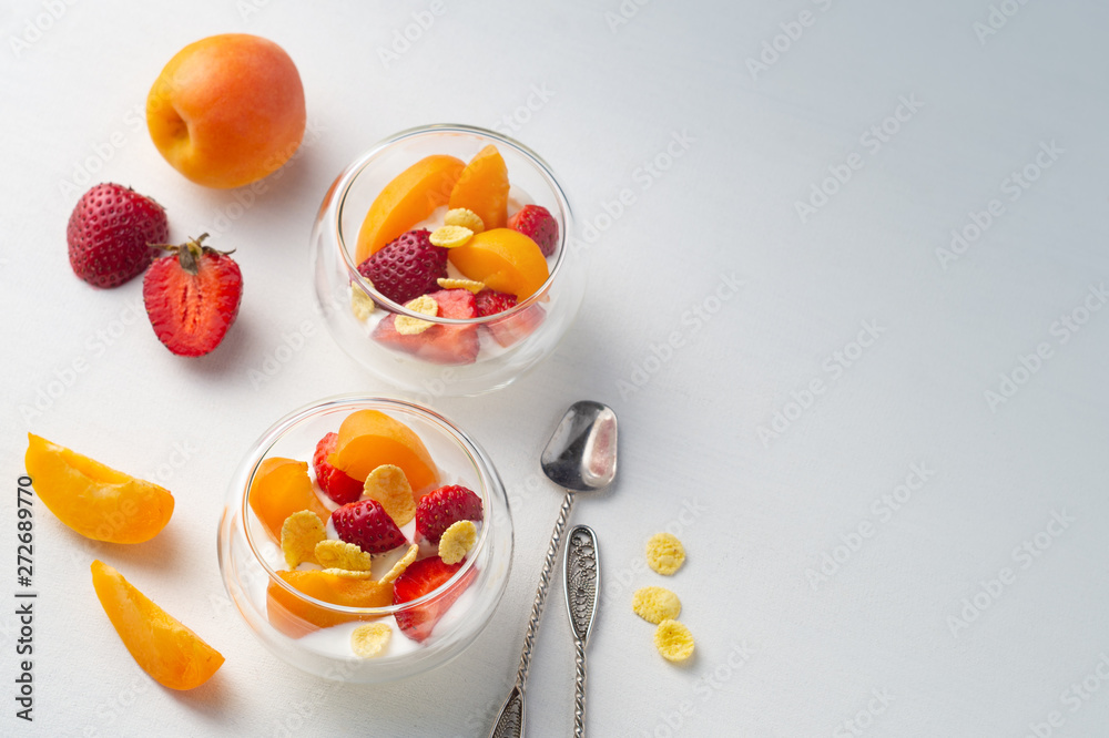Light vitamin healthy dessert of sliced strawberry, apricot and cornflakes with cream in glass creamers