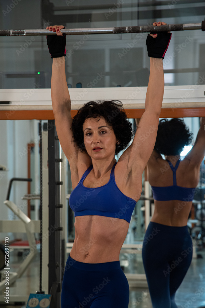 Half-length portrait of a young muscular girl with a blue bodice, she uses multipower in the gym. Concept of fitness, sport, training, gym and lifestyle.