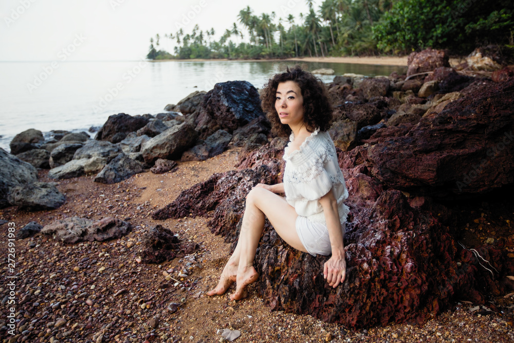 Young asian woman sitting on the coast of a tropical sea beach.