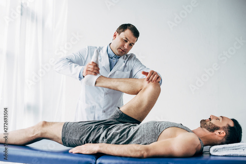 handsome chiropractor stretching leg of patient in hospital