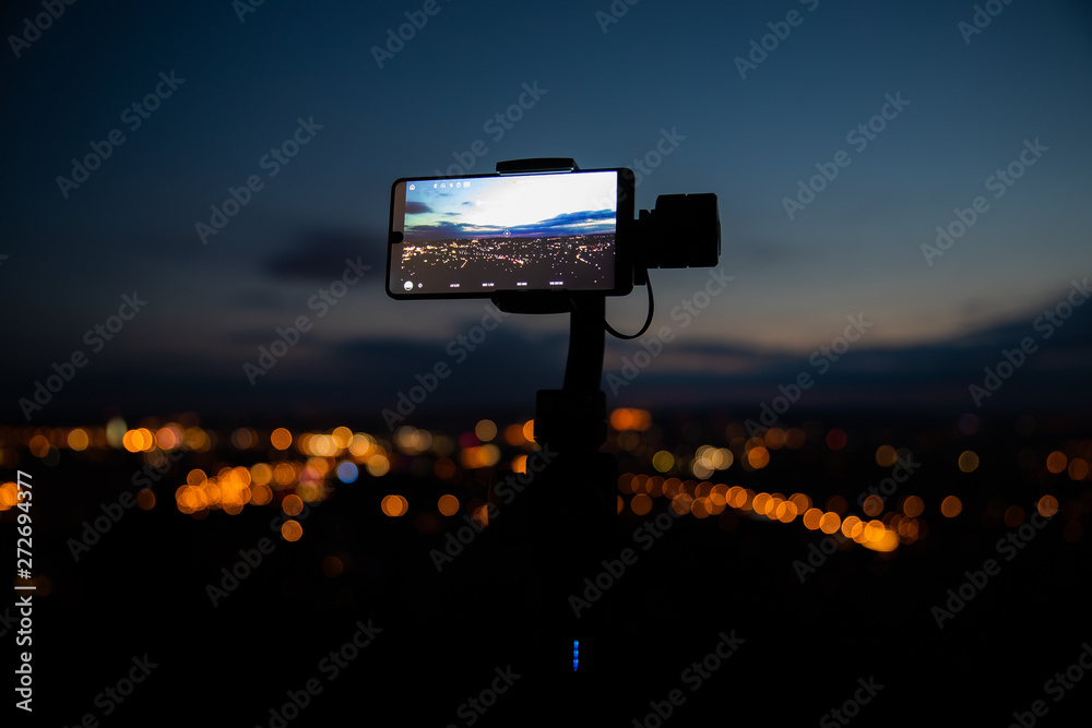 Fototapeta premium Mobile phone taking pictures on colorful sunset on Bila Hora with amazing view on city Brno Czech Republic pink and orange colors with many clouds and city lights