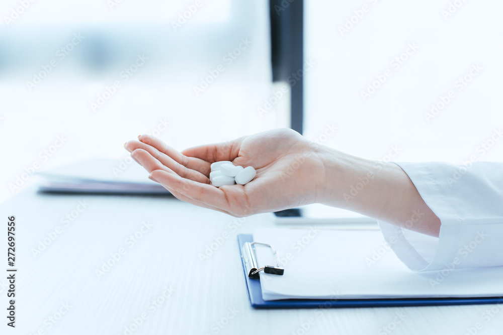 cropped shot of doctor with handful of pills near clipboard on table