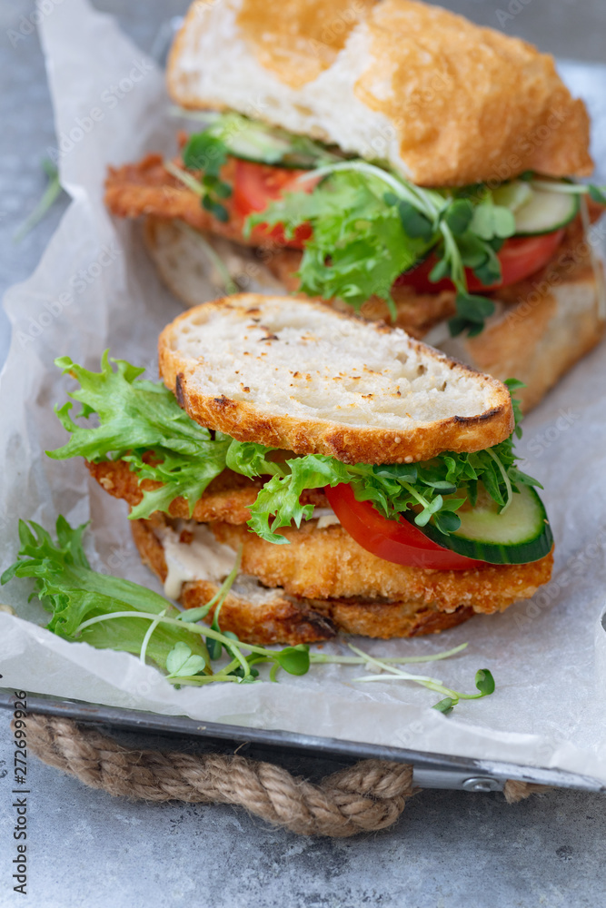 Sanwich with fried chicken on chiabatta with tomatoes, cheddar cheese, cucumber, onion, salad and microgreens