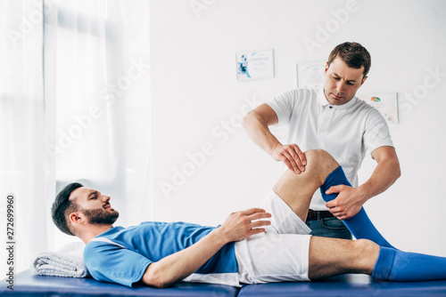 Fototapeta Naklejka Na Ścianę i Meble -  Physiotherapist massaging leg of football player lying on massage table in hospital