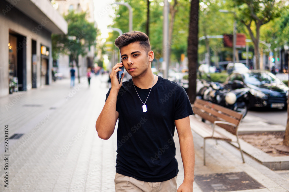 Young fashionable handsome man on the street of modern city talking on a cell phone. Communication concept