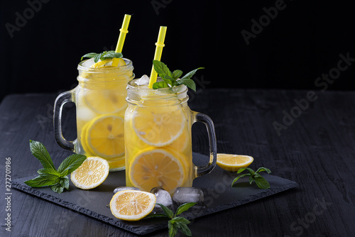 Lemonade in a jar with ice and mint on a black wooden table.