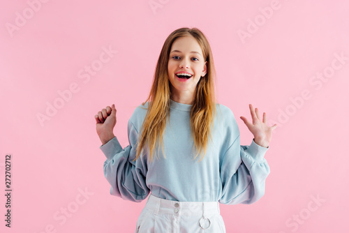 happy pretty teenage girl looking at camera isolated on pink
