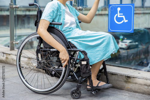 Young disabled woman in wheelchair near handicapped walkway sign, transportation convenience for disabled people concept.