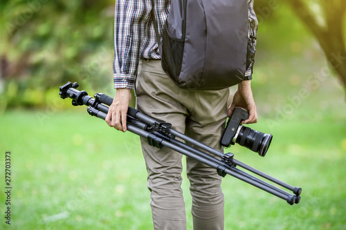 A photographer or traveller with a camera tripod in the nature for background.