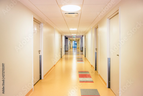Long hospital corridor with light walls, colorful floor and ceiling with plafone lamps illuminated. Health care and medical background concept.