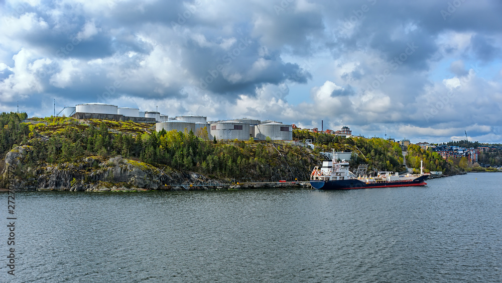 Oil/Chemical tanker sit berthed at a shore terminal with a oil product storage tanks above on Stockholm archipelago coast.
