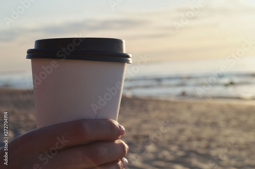 man holds in his hand a cup of coffee, tea, in the background a beautiful sunset on the sea