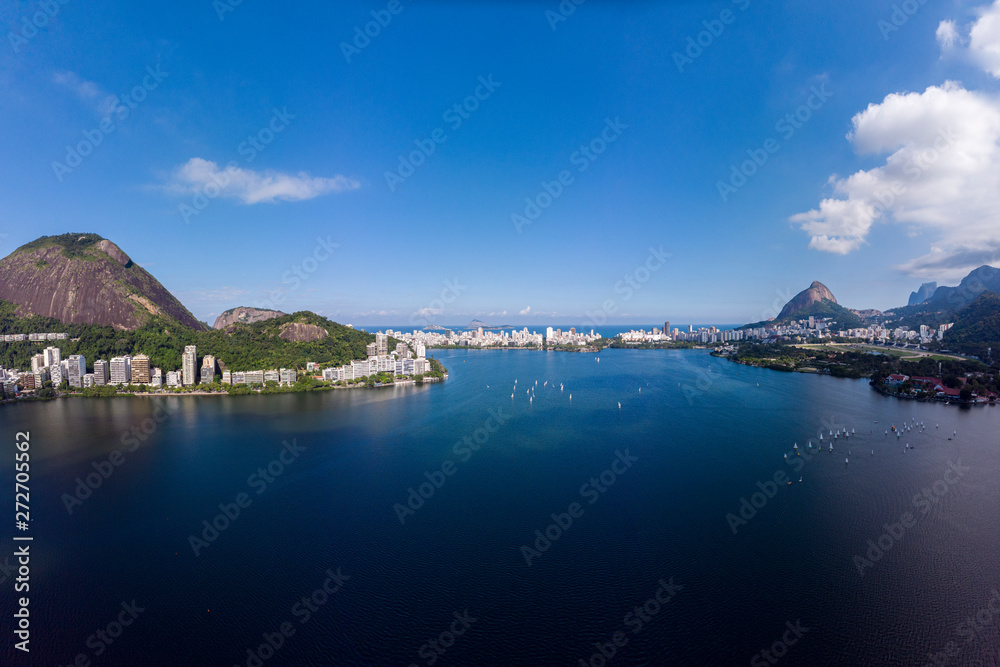 Aerial view of the city lake Lagoa Rodrigo de Freitas in Rio de Janeiro with a sailboat race while clouds coming in on a bright day with blue sky.
