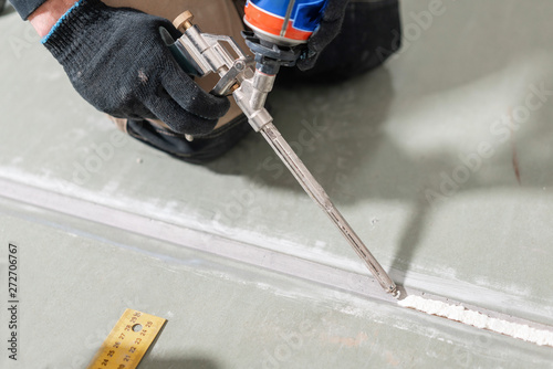 Worker is using a polyurethane foam for gluing drywall at ninety degrees. Hand holding polyurethane expanding foam glue gun applicator photo
