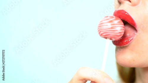 close-up, female sexy lips with red lipstick suck big pink round lollipop. copy space. blue background