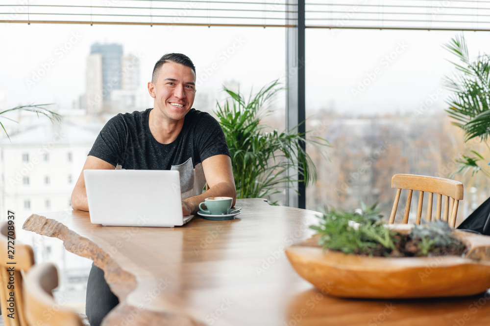 Successful people, businessman in comfortable cafe. Freelancer work on netbook in modern coworking. Young man drinking coffee from a Cup. Programmer at remote job. High large Windows