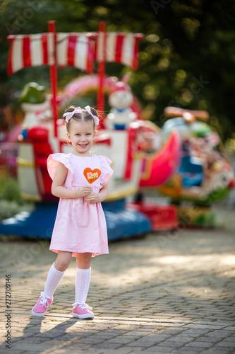 happy cute sweet girl 4-5 years old amid rides in the park eating tasty candy