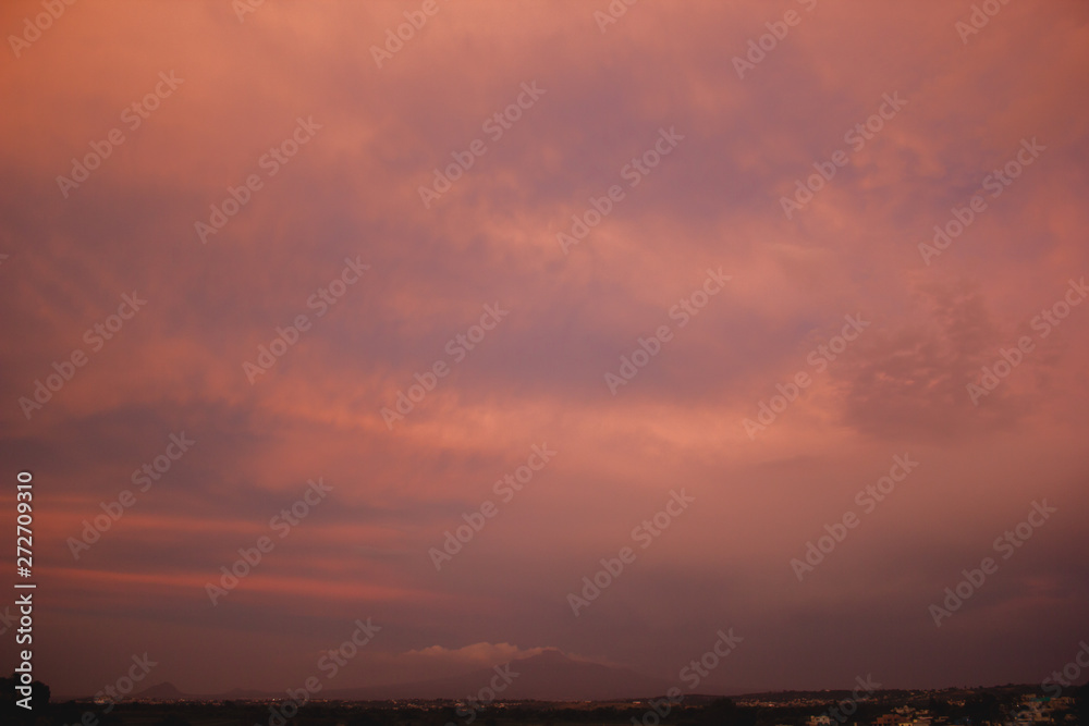 A BEAUTIFUL SUNSET SKY WITH ORANGE AND YELLOW CLOUDS WITH BLUE SKY WITH A MOUNTAINS ON THE BOTTOM OF THE PICTURE