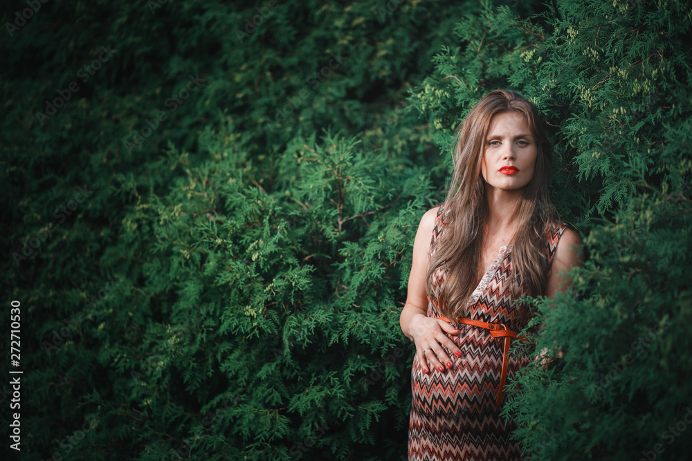 Young pregnant woman in the park outdoors. Calm pregnant woman in third trimester. Walking in public garden. Trees in the forest Young pregnant woman in the park outdoors. Calm pregnant woman in third trimester. Walking in public garden. Trees in the forest