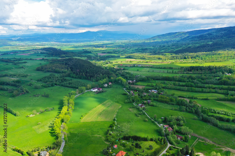 Aerial perspective view on sudety mountains during cloudy day with villages in the valley surrounded by meadows, forest and rapeseed fields