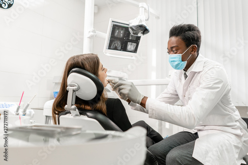 Doctor treats teeth. Young African male dentist with a patient. Woman in the dentist chair at dental clinic. Medicine  health  stomatology concept. dentist treating a patient.