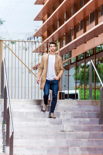 A young man descends by the stairs in the city wearing a coat.
