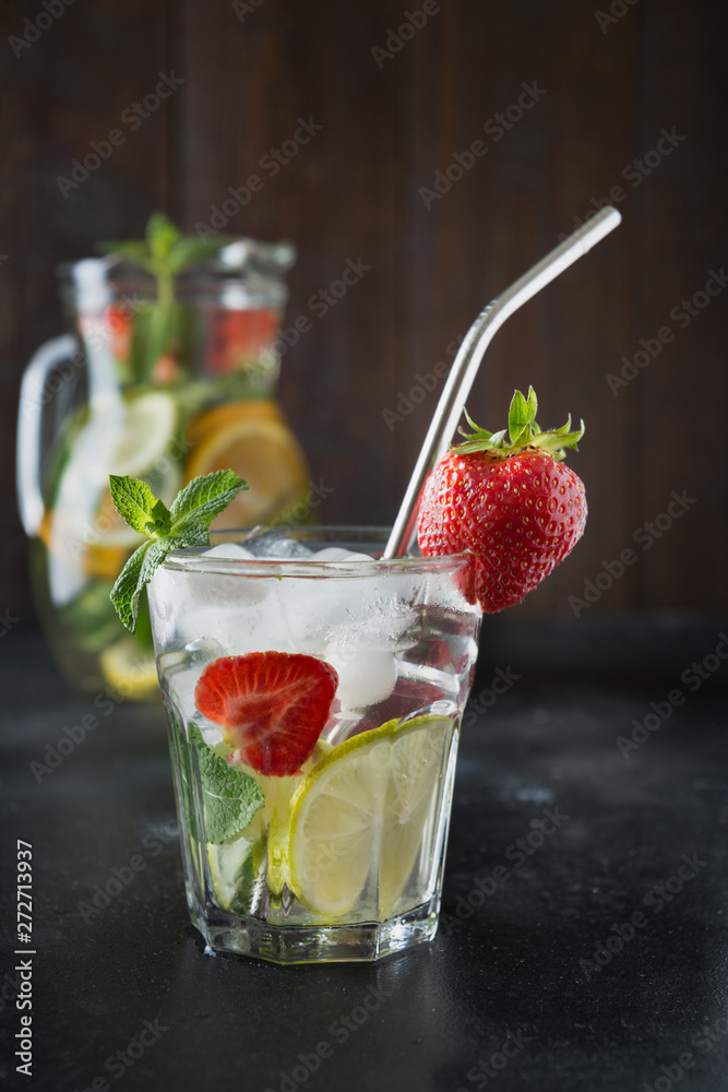 Detox lemonade with lime, orange, lemon, strawberry in glass and jug. Summer healthy freshness drink. Dark wooden background. Detox lemonade with lime, orange, lemon, strawberry in glass and jug. Summer healthy freshness drink. Dark wooden background.
