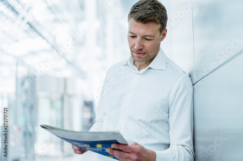 Businessman leaning against a wall reading newspaper