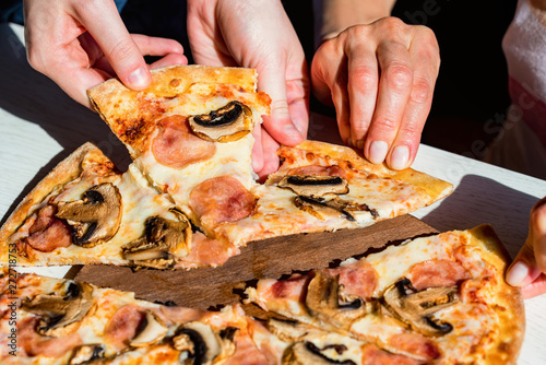 Fotografie Hands take slices of fresh pizza with salami, mushrooms and cheese close up