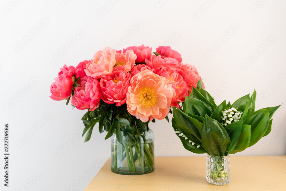 Coral peonies and spring lilies of the valley in a glass vase on wooden table.. Beautiful peony flower for catalog or online store. Floral shop concept . Beautiful fresh cut bouquet. Flowers delivery. Coral peonies and spring lilies of the valley in a glass vase on wooden table.. Beautiful peony flower for catalog or online store. Floral shop concept . Beautiful fresh cut bouquet. Flowers delivery.