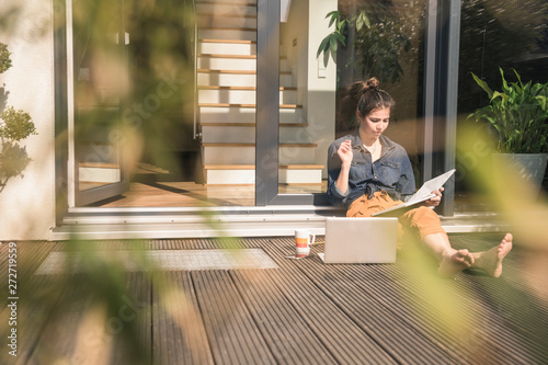 Young woman sitting on terrace at home working with book and laptop photo