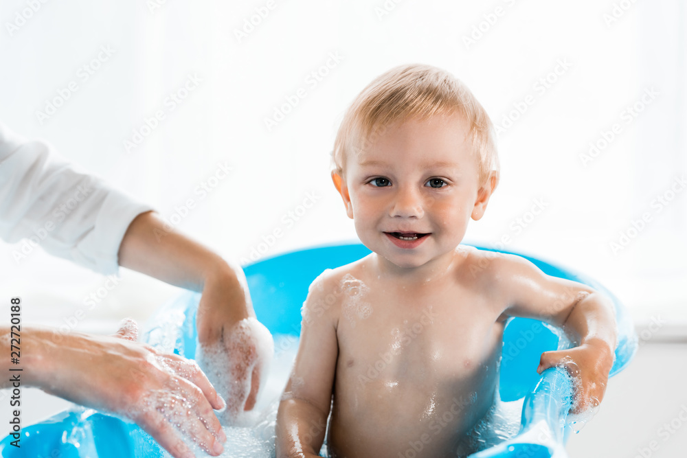 cropped view of mother near happy toddler child in blue baby bathtub cropped view of mother near happy toddler child in blue baby bathtub